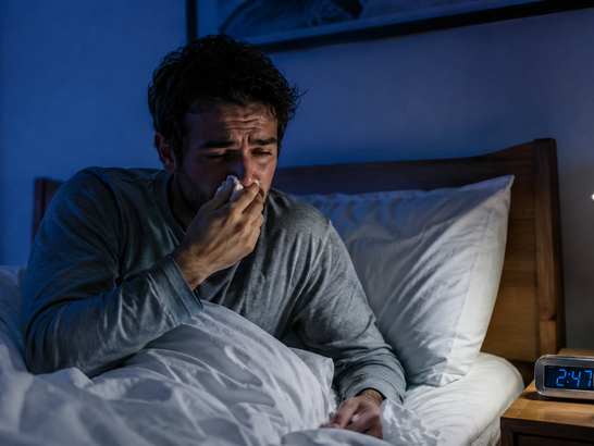 Persona despierta de madrugada en la cama con congestión nasal y expresión de cansancio